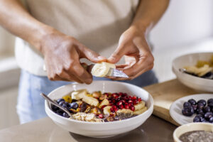close up of person making healthy breakfast in kitchen with fruits and yogurt