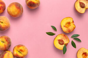Ripe juicy peaches with green leaves on pink background. Flat lay, top view, copy space. Minimal creative composition with peaches. Fresh organic fruit, vegan food. Harvest concept