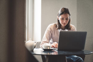 A female student sitting alone in a coffeeshop, using her computer to work on the go, writing her diploma and studying for exams, drinking tea.